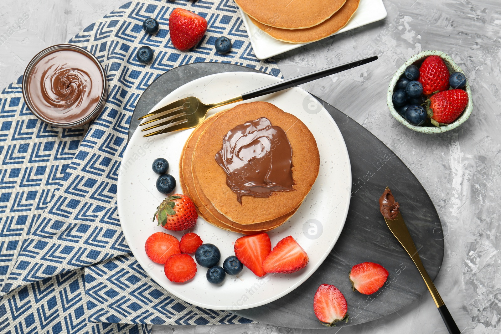 Photo of Tasty pancakes with chocolate paste and berries served on grey table, flat lay