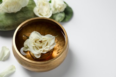 Photo of Tibetan singing bowl with water and beautiful rose flowers on white background, space for text