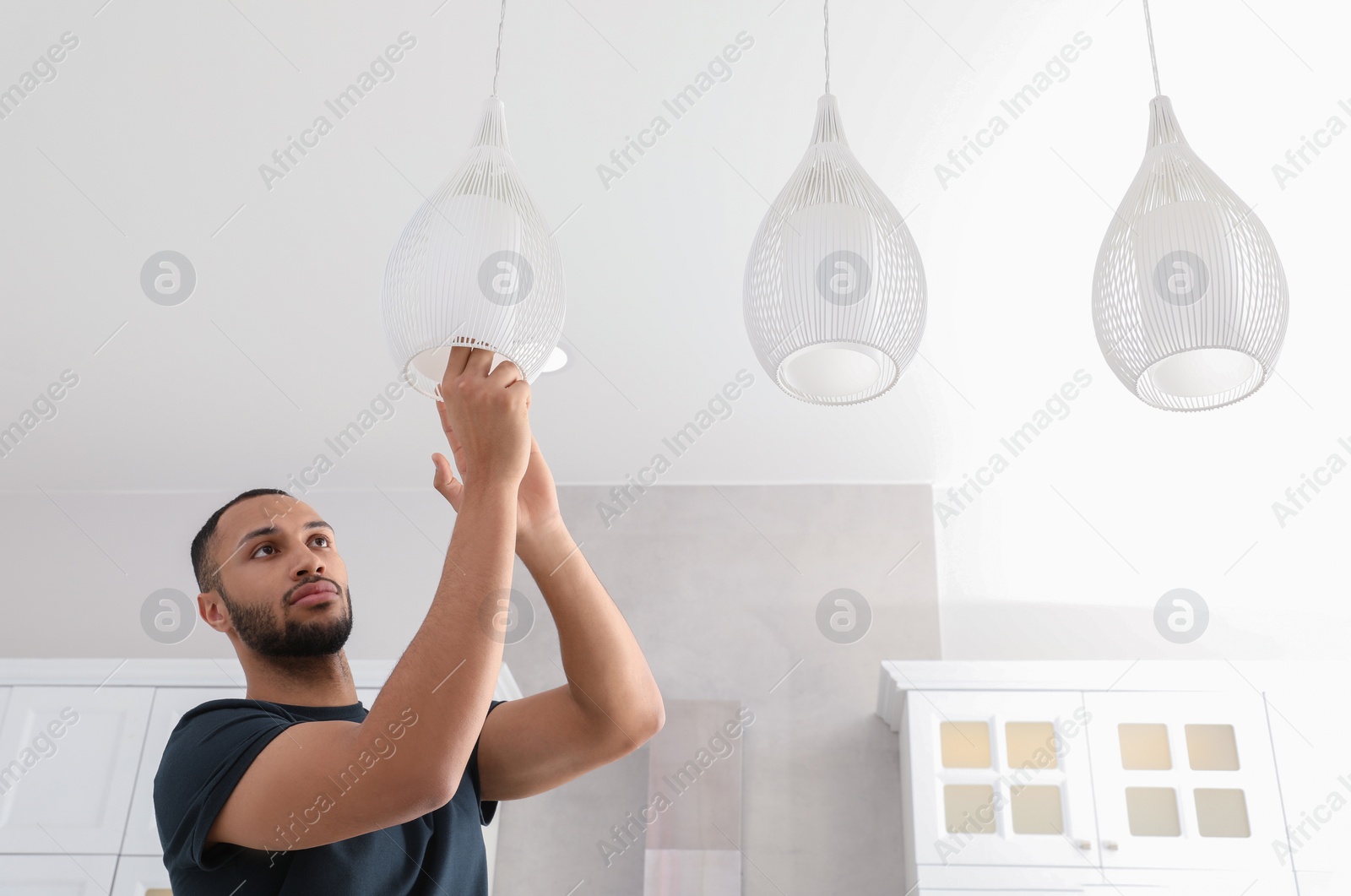 Photo of Young man repairing ceiling lamp indoors, space for text