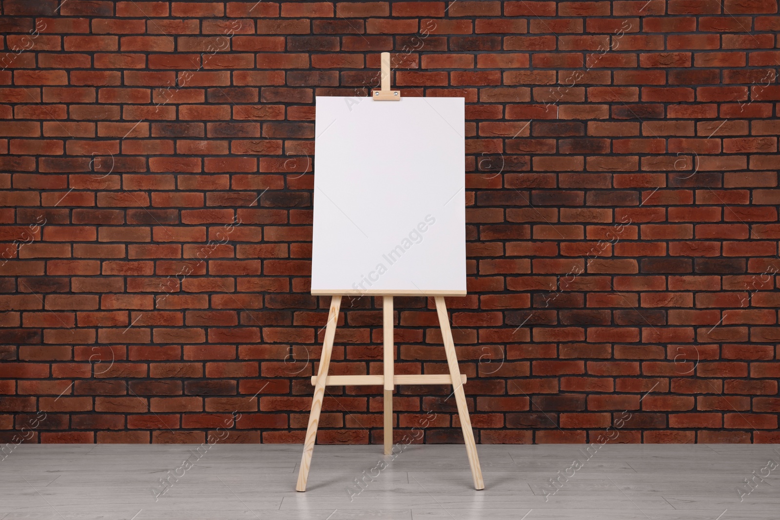 Photo of Wooden easel with blank canvas near brick wall indoors