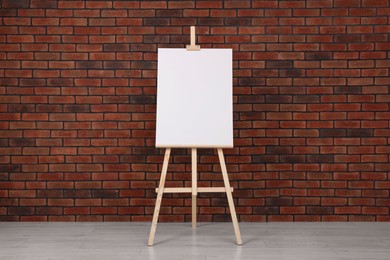 Photo of Wooden easel with blank canvas near brick wall indoors