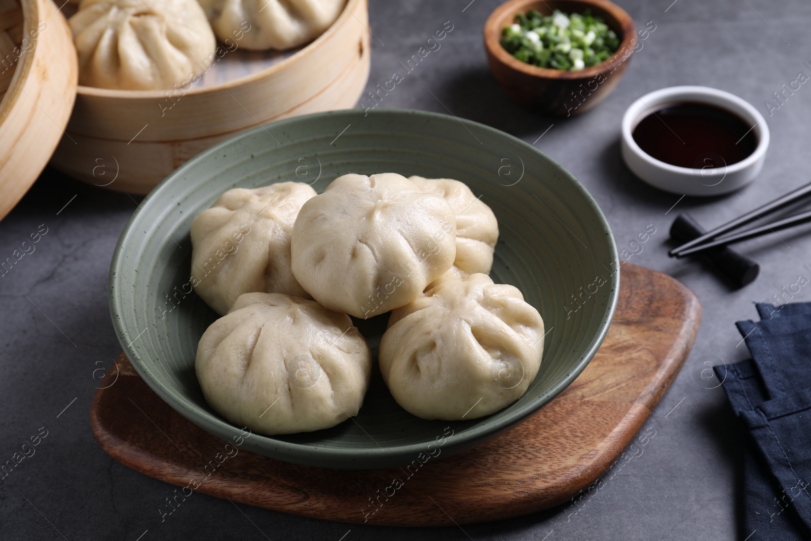 Photo of Delicious bao buns (baozi) in bowl on grey table, closeup