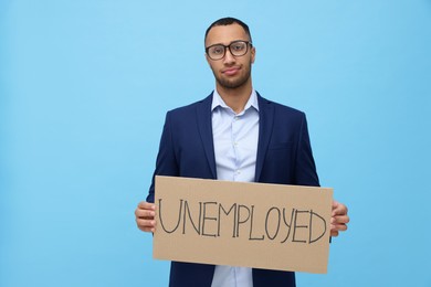 Young man holding sign with word Unemployed on light blue background