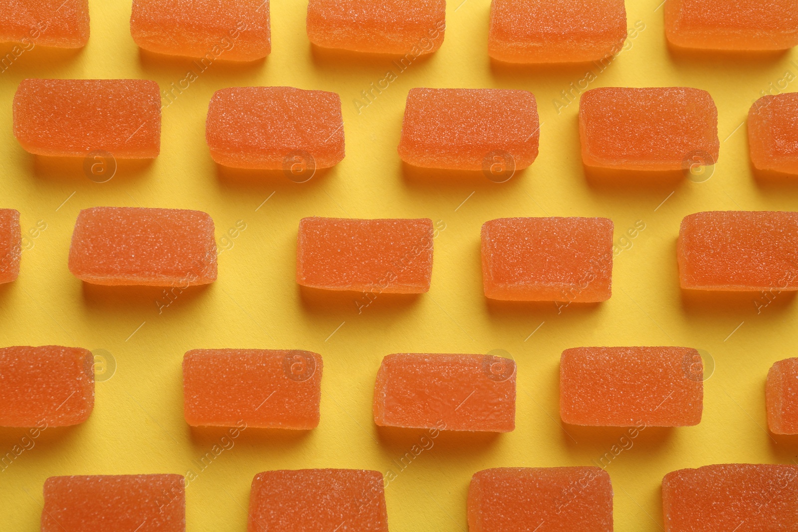 Photo of Tasty orange jelly candies on yellow background, flat lay