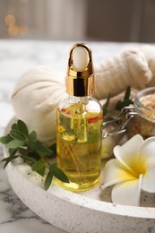 Beautiful spa composition with essential oil and plumeria flower on white marble table, closeup