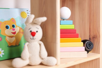 Photo of Small camera hidden among toys on wooden shelf in baby room