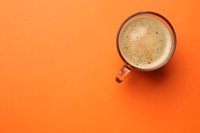 Photo of Fresh coffee in cup on orange background, top view. Space for text