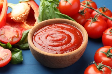 Bowl of tasty ketchup and ingredients on blue wooden table, closeup