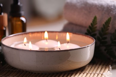 Photo of Spa composition. Burning candles in bowl, towels and bottles of essential oil on table, closeup