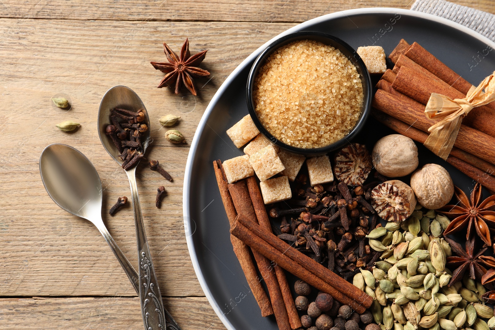 Photo of Plate with different aromatic spices and spoons on wooden table, flat lay