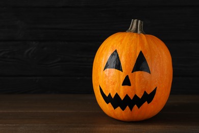 Photo of Pumpkin with drawn spooky face on wooden table, space for text. Halloween celebration