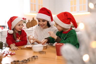 Mother and her cute little children decorating tasty Christmas cookies at table in kitchen