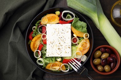 Photo of Bowl of tasty salad with leek, cheese and olives served on wooden table, flat lay