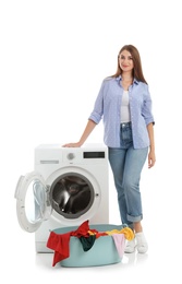 Young woman near washing machine and basket with laundry on white background