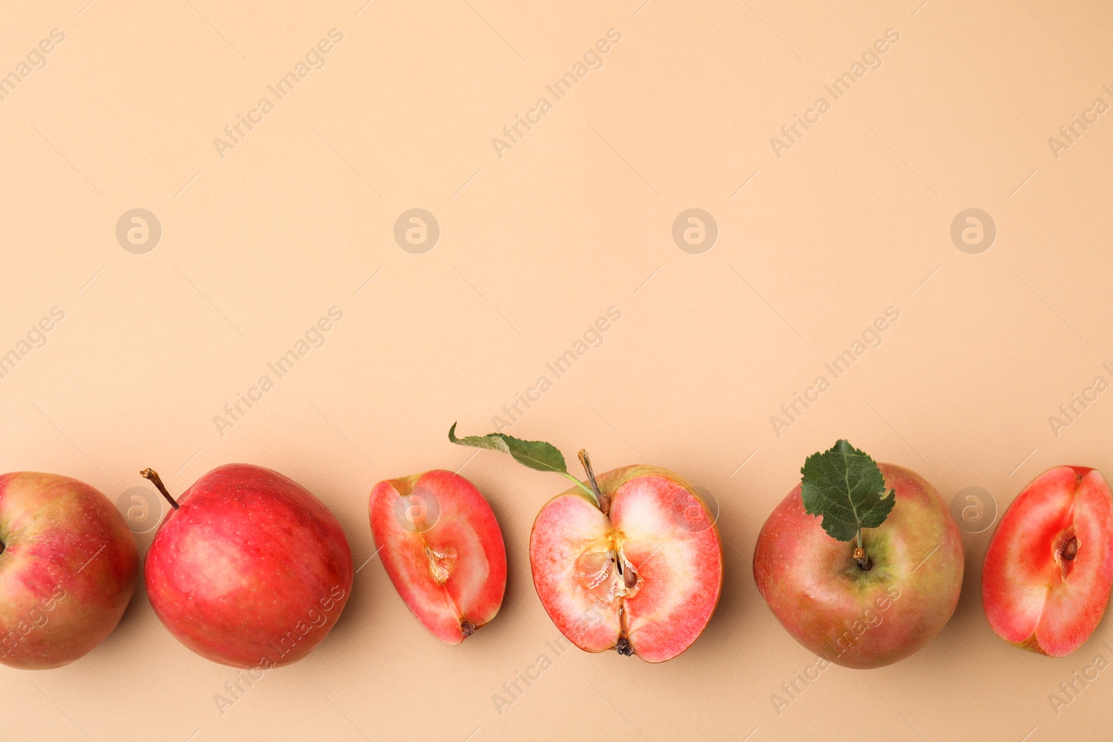Photo of Tasty apples with red pulp and leaves on beige background, flat lay. Space for text