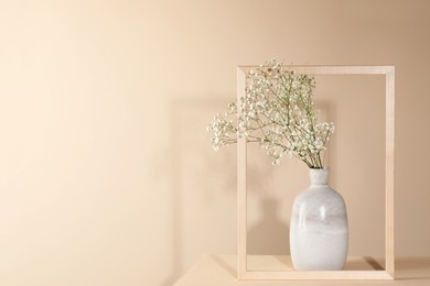 Photo of Vase with flowers and picture frame on wooden table against beige background, space for text