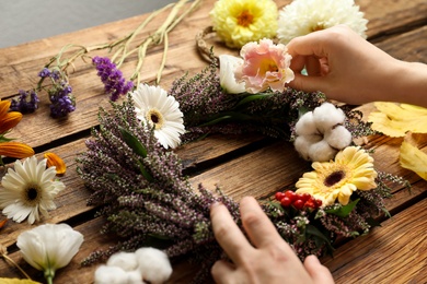 Florist making beautiful autumnal wreath with heather flowers at wooden table, closeup
