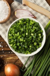 Photo of Chopped green onion in bowl on wooden table, flat lay