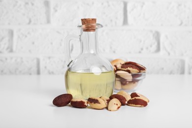 Photo of Tasty Brazil nuts and bottle with oil on white table against brick wall