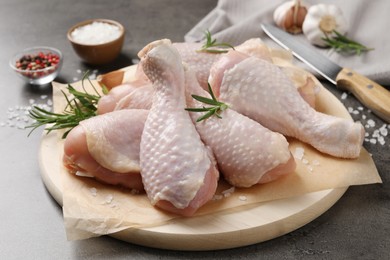 Photo of Wooden board with fresh raw chicken legs and other products on grey table