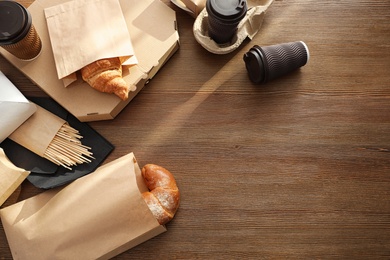 Paper bags with pastry and takeaway food on wooden table, top view. Space for text