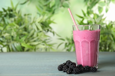 Photo of Tasty fresh milk shake with blackberries on light blue wooden table against blurred background, space for text