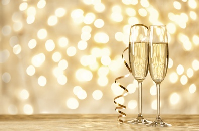 Photo of Glasses of champagne on table against blurred lights. Space for text