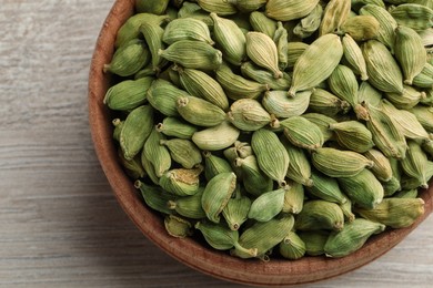 Bowl of dry cardamom pods on white wooden table, top view