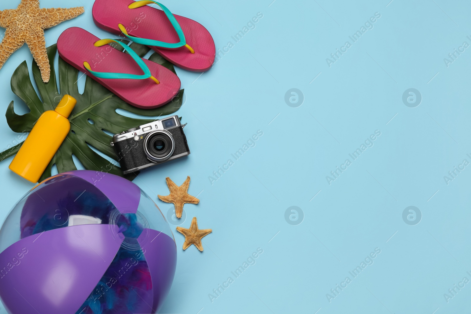 Photo of Inflatable ball and beach accessories on light blue background, flat lay. Space for text