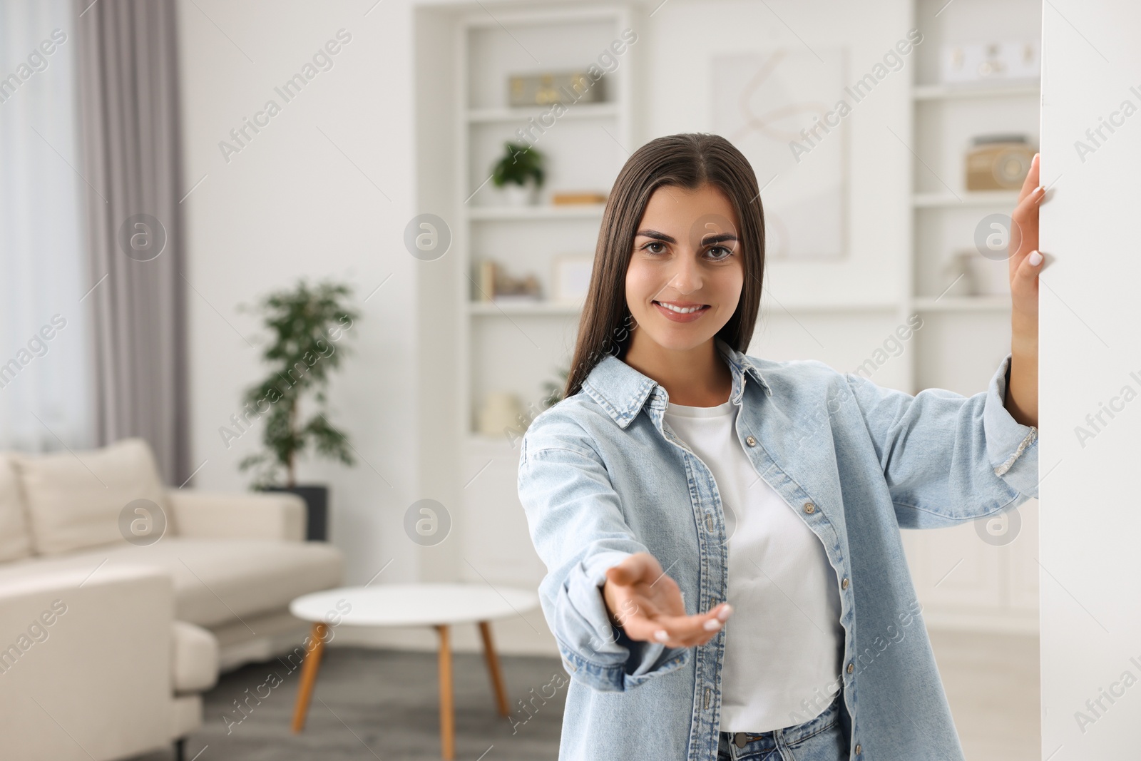 Photo of Happy woman welcoming near white wall at home, space for text. Invitation to come in room