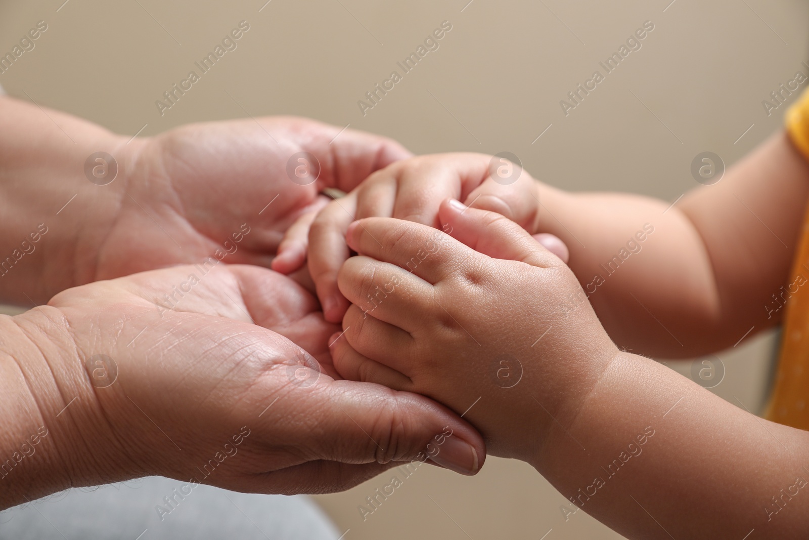 Photo of Woman holding hands with her granddaughter on beige background, closeup