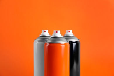 Photo of Colorful cans of spray paints on orange background, closeup