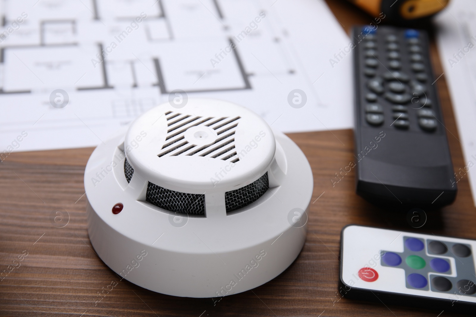 Photo of Smoke detector and remote controls on wooden table, closeup. Home security system