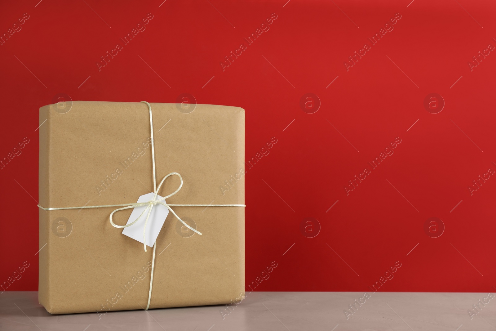 Photo of Parcel wrapped in kraft paper with tag on table against red background, space for text