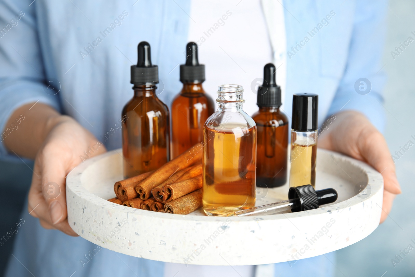 Photo of Woman holding tray with different bottles of essential oils, closeup