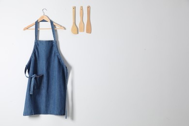 Photo of Denim apron and kitchen tools on light wall. Space for text