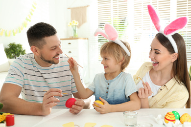 Happy father, mother and son having fun while painting Easter eggs at table indoors