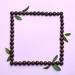 Frame made with acai berries and green leaves on violet background, flat lay. Space for text