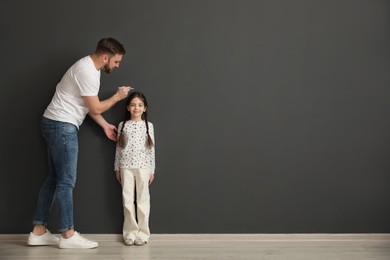 Photo of Father measuring daughter's height near black wall indoors, space for text
