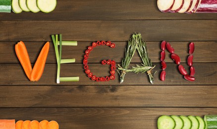 Image of Word VEGAN made of different fresh tasty vegetables on wooden background, flat lay