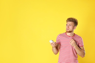 Photo of Young man with air conditioner remote suffering from heat on yellow background. Space for text
