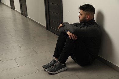 Photo of Sad man sitting on floor in hall. Space for text