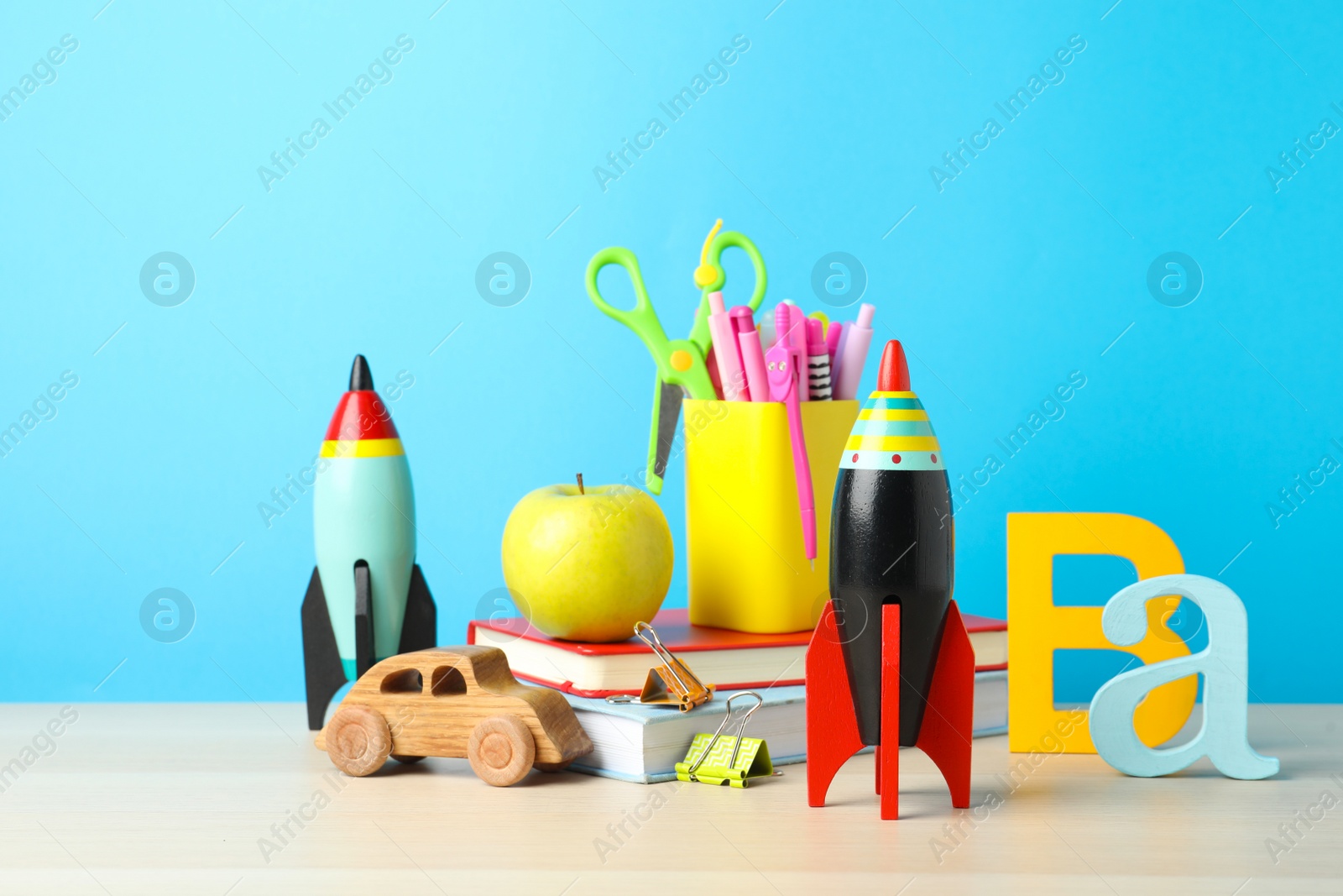 Photo of Bright toy rockets, car and school supplies on wooden table