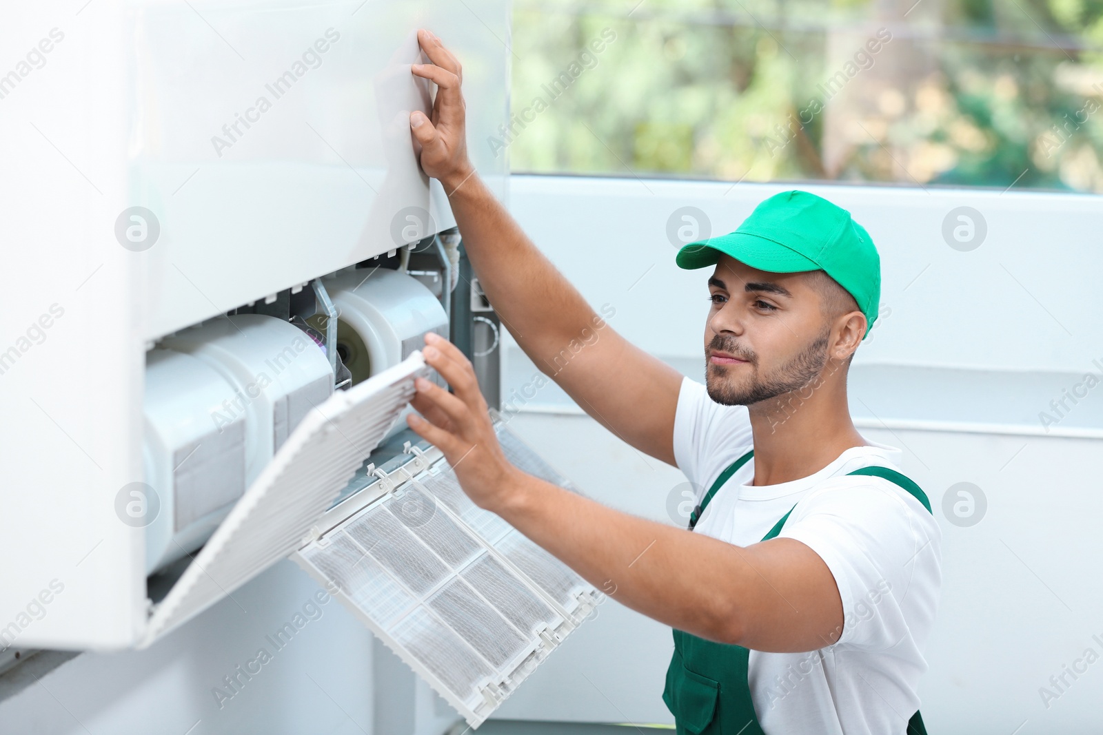 Photo of Professional technician maintaining modern air conditioner indoors