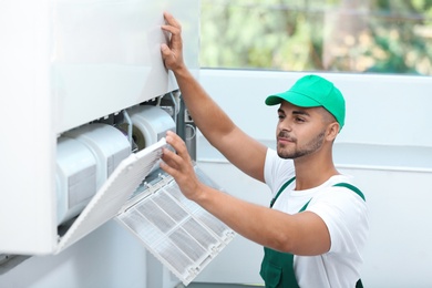 Professional technician maintaining modern air conditioner indoors