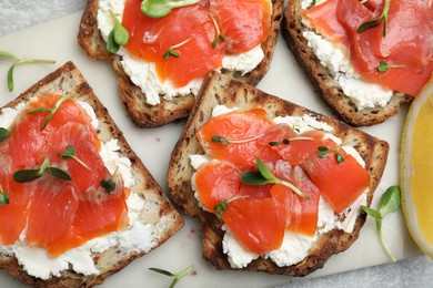 Photo of Delicious sandwiches with cream cheese, salmon and microgreens on white marble board, top view