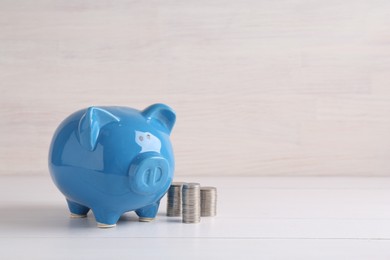 Photo of Financial savings. Piggy bank and stacked coins on white wooden table, space for text