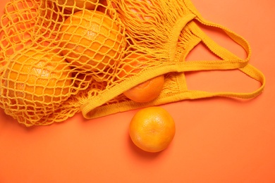 Photo of Net bag with citrus fruits on coral background, flat lay