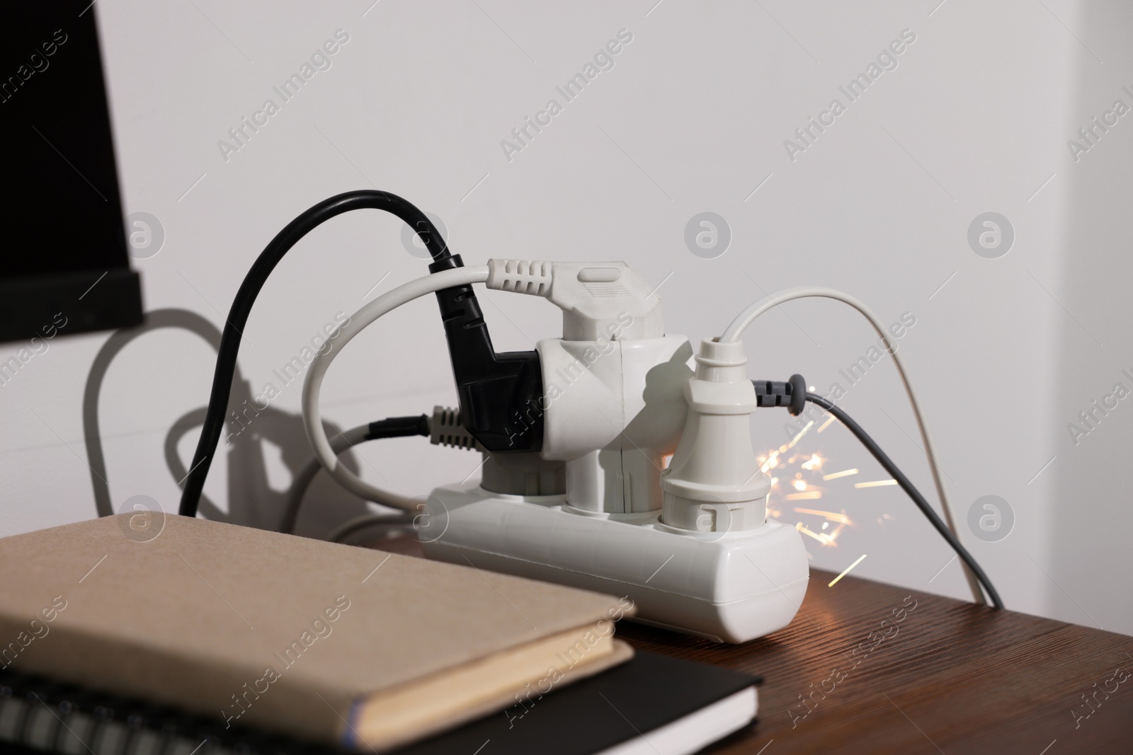 Photo of Inflamed plug in power strip indoors on wooden table. Electrical short circuit