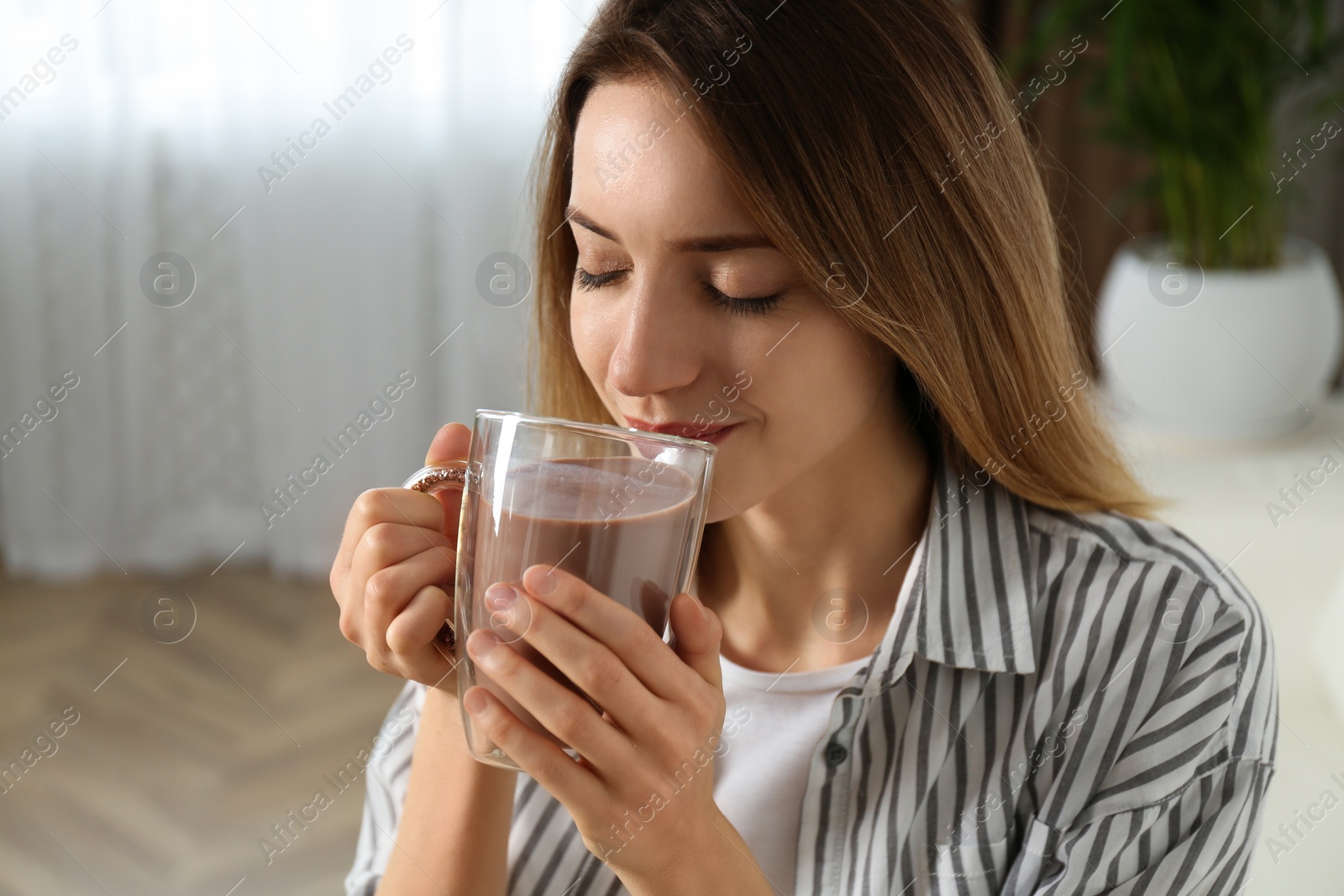 Photo of Young woman drinking chocolate milk in room